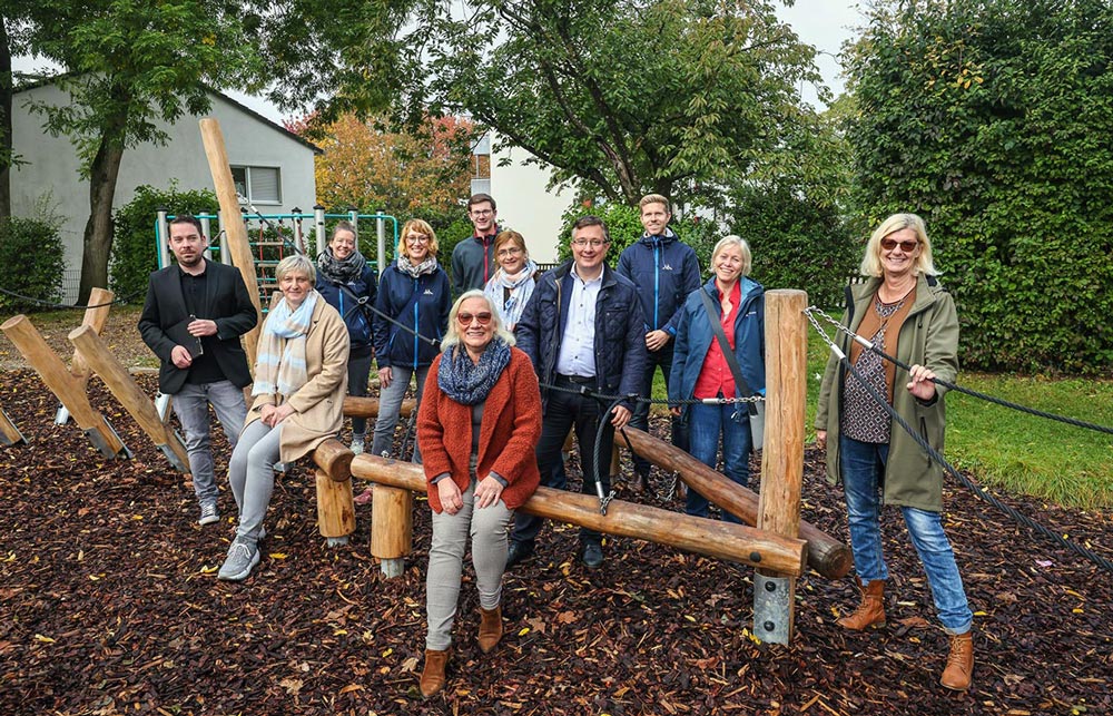 Fröhliches Gruppenfoto von elf Erwachsenen am Klettergerüst der Filchnerschule in Mülheim.