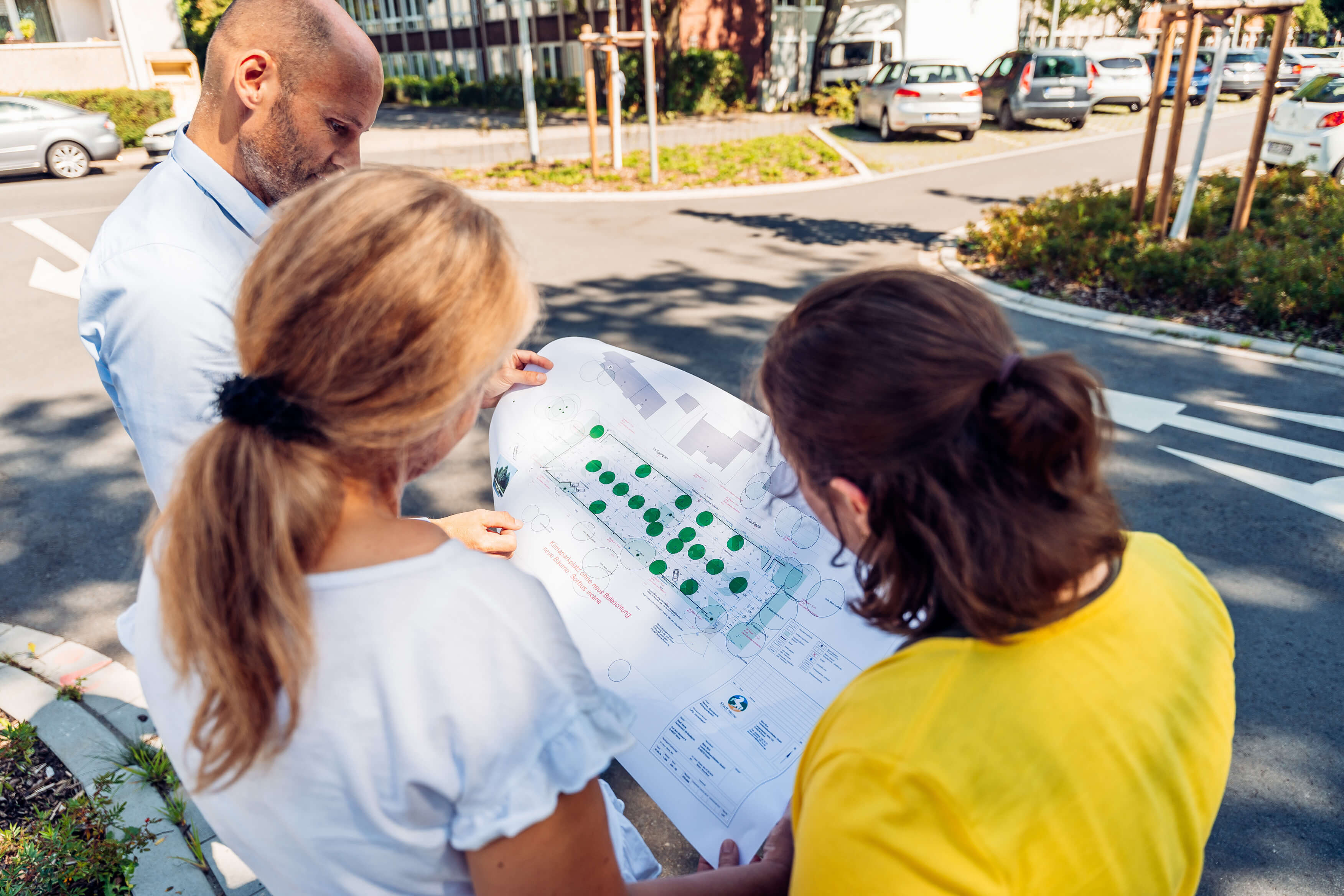 Drei Menschen schauen auf den Bauplan des Klimaparkplatzes in Herne