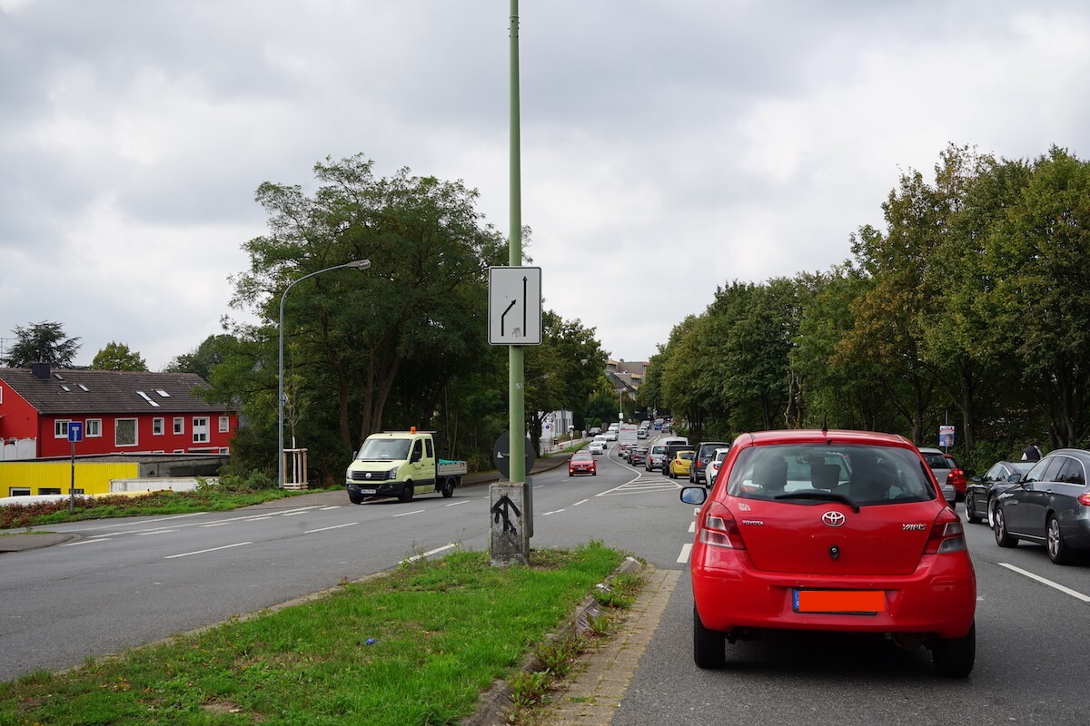 Autos fahren auf einer viel befahrenen zweispurigen Straße. Im Bildfokus ist ein roter Kleinwagen. 