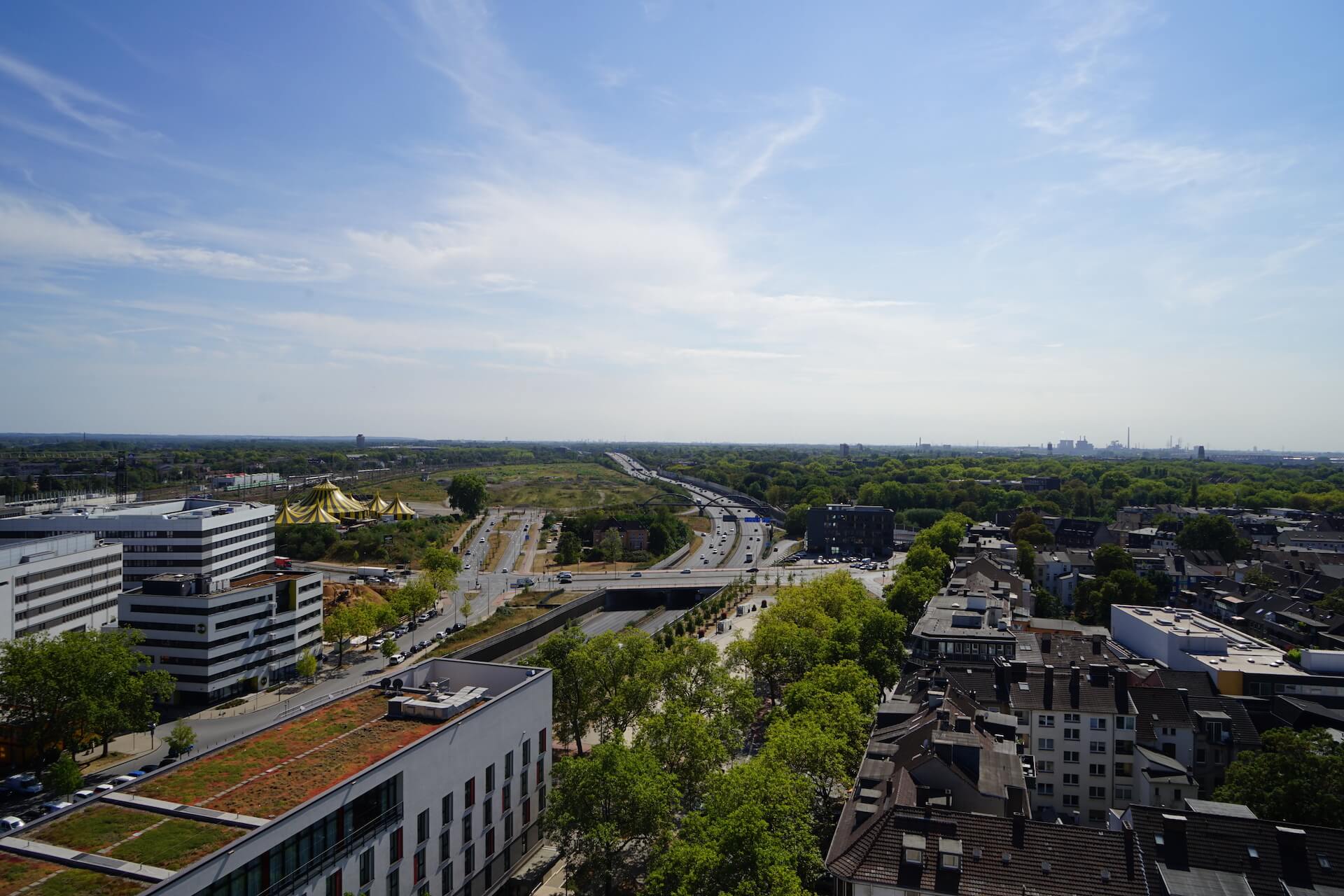 Zu sehen ist eine Luftaufnahme der Skyline vom Ruhrgebiet, blauer Himmel und eine Autobahn. 