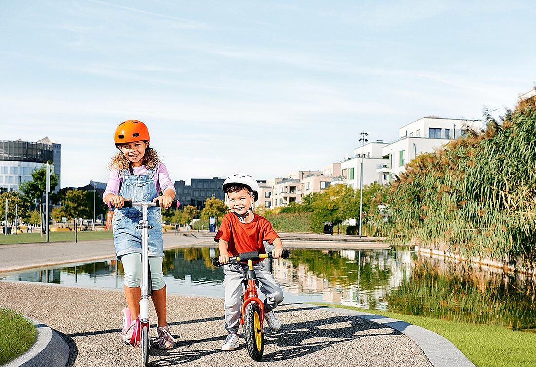 Junges Geschwisterpaar fährt Roller und Fahrrad im Park.